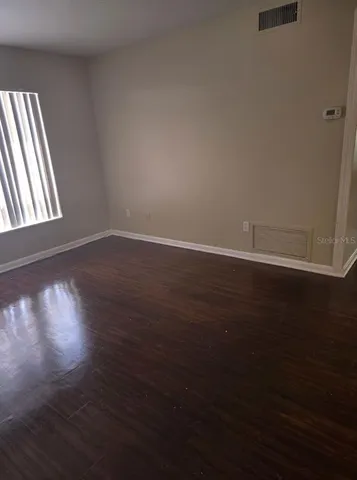 a view of an empty room with wooden floor and a window