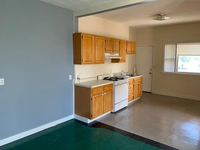 a view of an empty room with a window and a kitchen