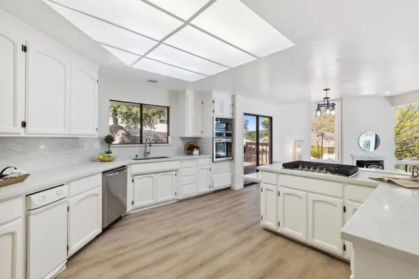 a large kitchen with a stove a sink dishwasher and white cabinets with wooden floor