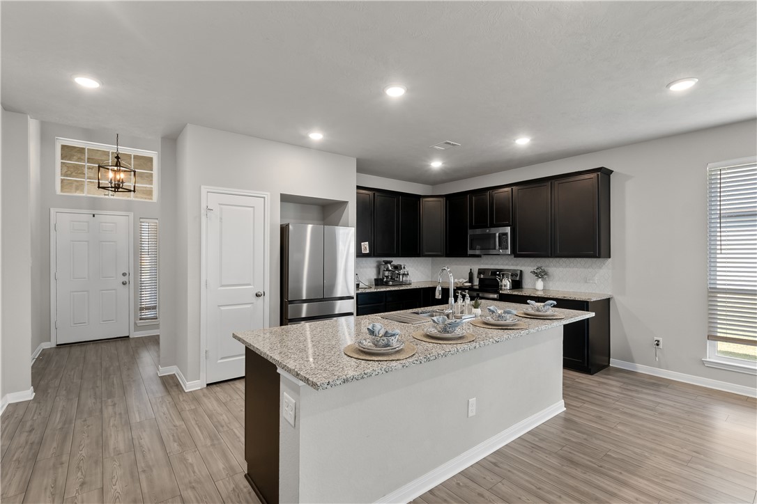 1925 Viva Road Bryan, TX 77807 - Photo 2 of 25 Kitchen with stainless steel appliances, light stone countertops, light wood-style floors, a kitchen island with sink, and dark cabinetry