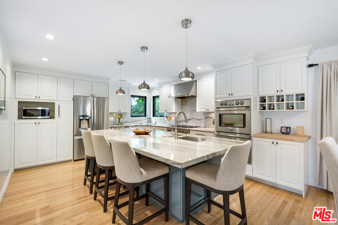 3558 Muirfield Road South Los Angeles, CA 90016 - Photo 14 of 35 a kitchen with stainless steel appliances a dining table chairs refrigerator and microwave