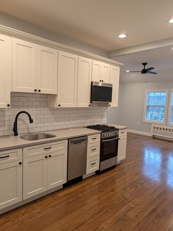 a kitchen with stainless steel appliances granite countertop a stove a sink and white cabinets with wooden floor