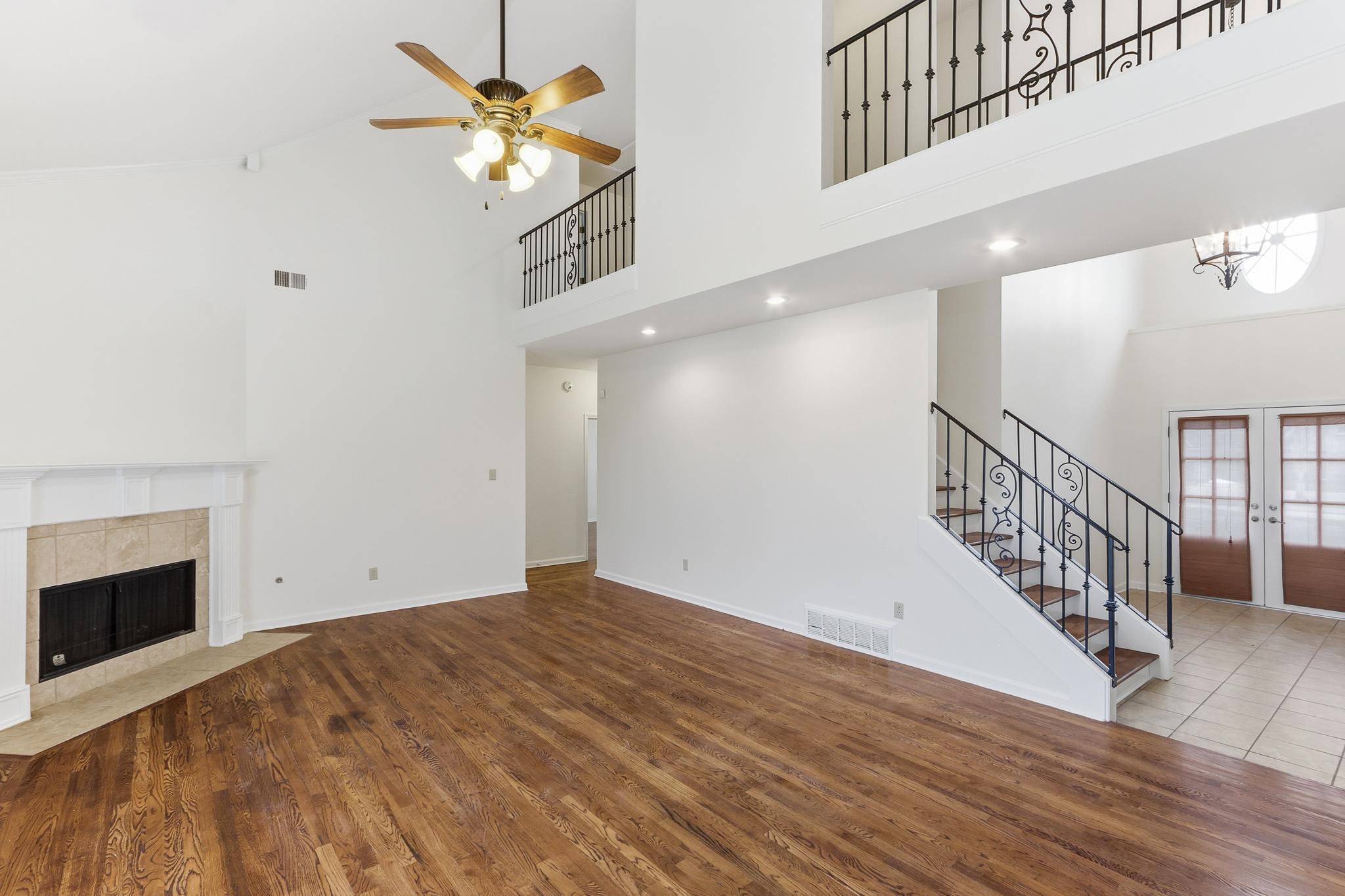 4854 Fox Springs Drive Collierville, TN 38017 - Photo 5 of 39 Unfurnished living room with a ceiling fan, wood finished floors, a tiled fireplace, and a high ceiling