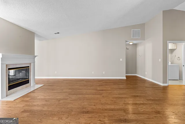 a view of an empty room with wooden floor fireplace and a window