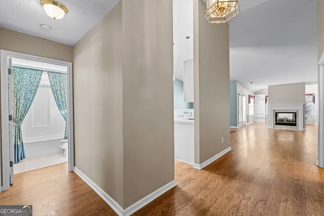 a view of a hallway to an empty room with wooden floor and a window