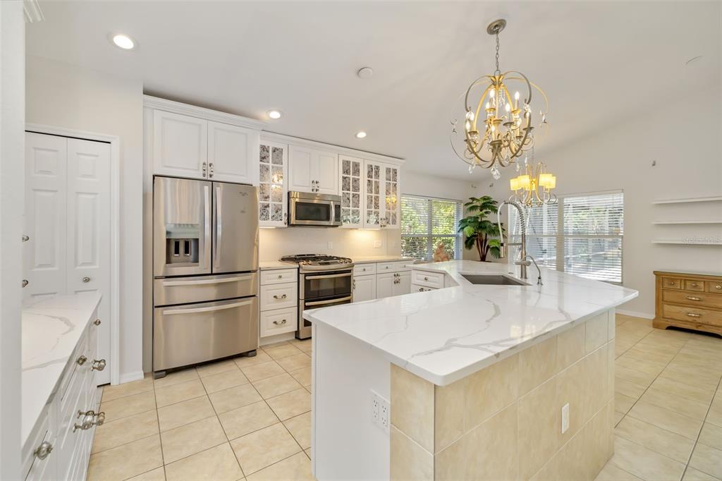 7631 Desert Inn Way Lakewood Ranch, FL 34202 - Photo 28 of 100 a large kitchen with stainless steel appliances kitchen island granite countertop a refrigerator a stove and a sink with chandelier