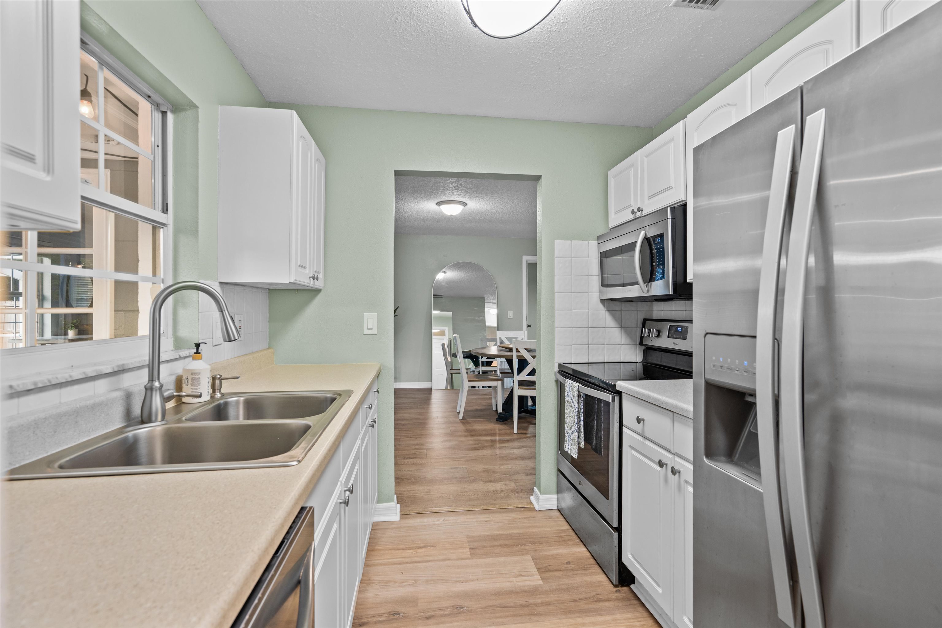 285 Trillo Street St. Augustine, FL 32086 - Photo 18 of 48 Kitchen featuring stainless steel appliances, white cabinets, a textured ceiling, light countertops, and arched walkways