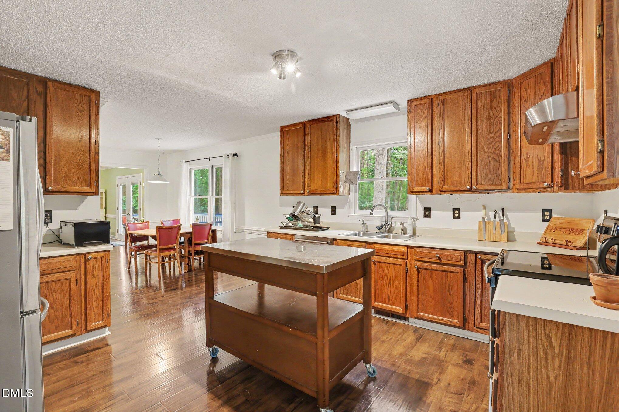 114 Oak Hollow Road Timberlake, NC 27583 - Photo 11 of 31 Kitchen featuring wood-finish flooring, wood cabinetry, light countertops, stainless steel sink, and a rolling island with a light countertop