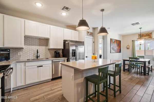 a kitchen with stainless steel appliances a stove a sink a refrigerator and white cabinets with wooden floor