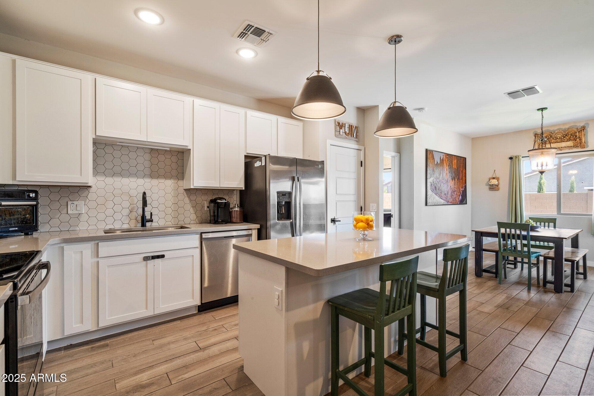 a kitchen with stainless steel appliances a stove a sink a refrigerator and white cabinets with wooden floor