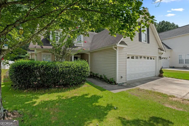 a view of a house with a yard plants and large tree