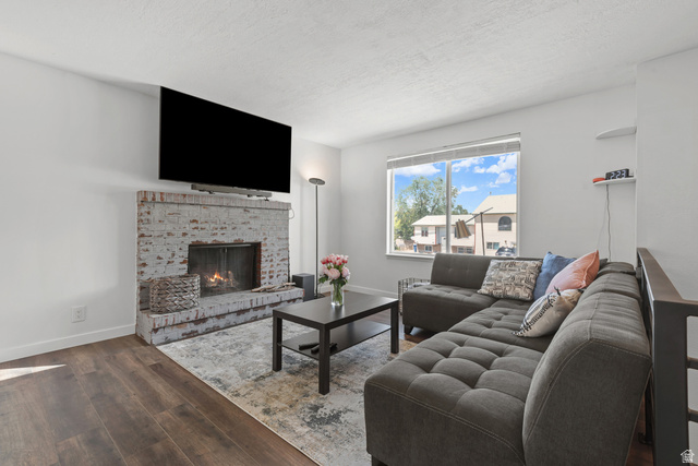 3951 Brixton Road Salt Lake City, UT 84129 - Photo 7 of 22 Living area featuring wood-finish flooring, a painted brick fireplace, a large picture window, and a built-in wall shelf