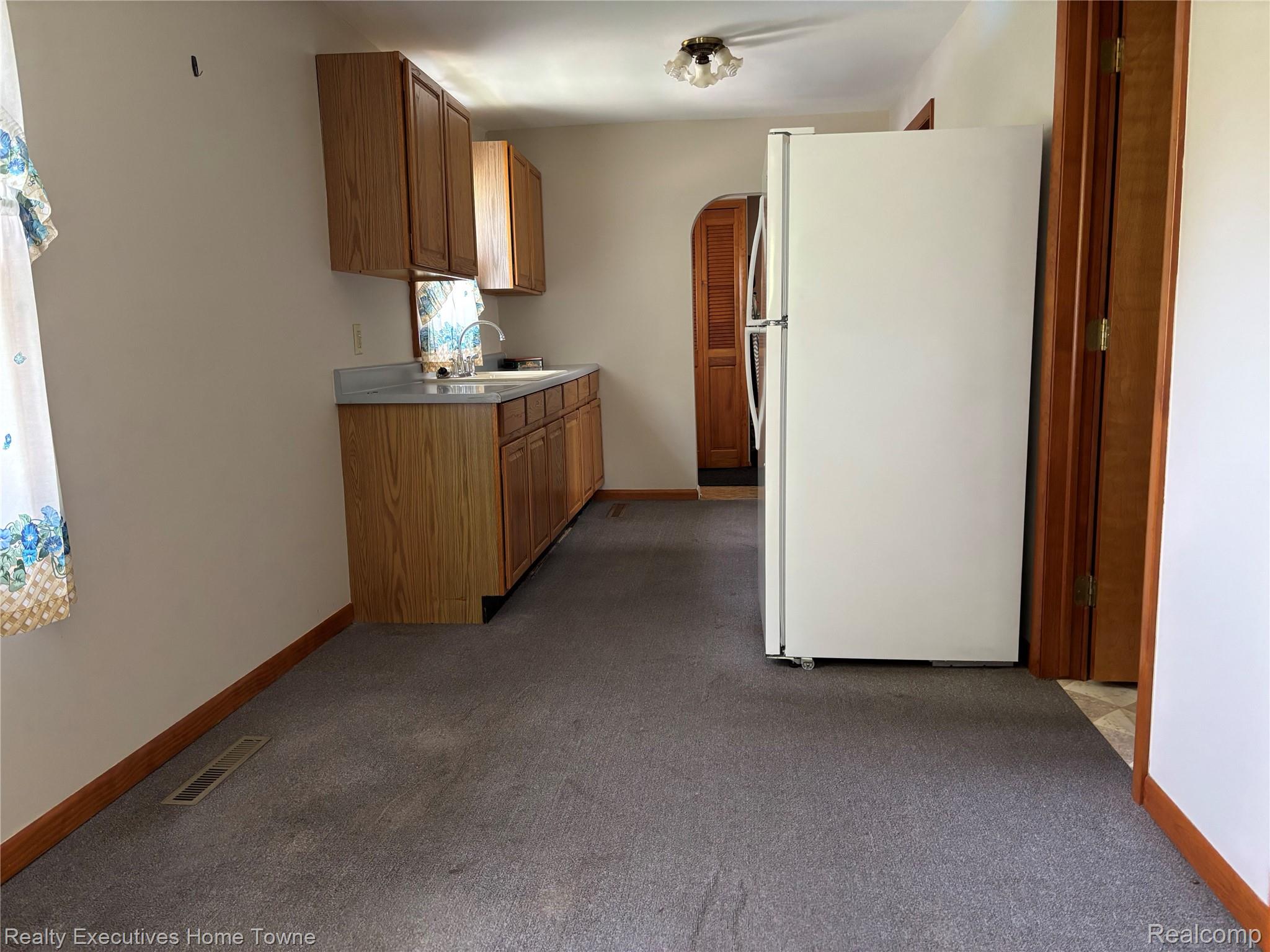 1782 Maple Road Smiths Creek, MI 48074 - Photo 23 of 30 Kitchen featuring freestanding refrigerator, dark colored carpet, arched walkways, light countertops, and wood finish cabinets