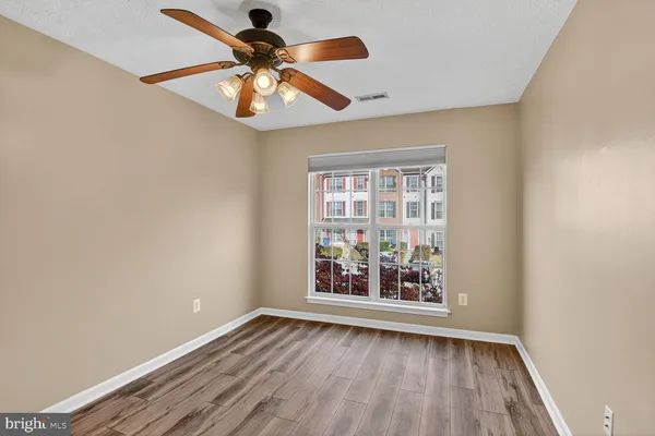 an empty room with wooden floor fan and windows
