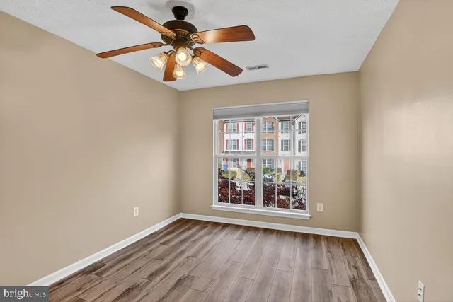 an empty room with wooden floor fan and windows