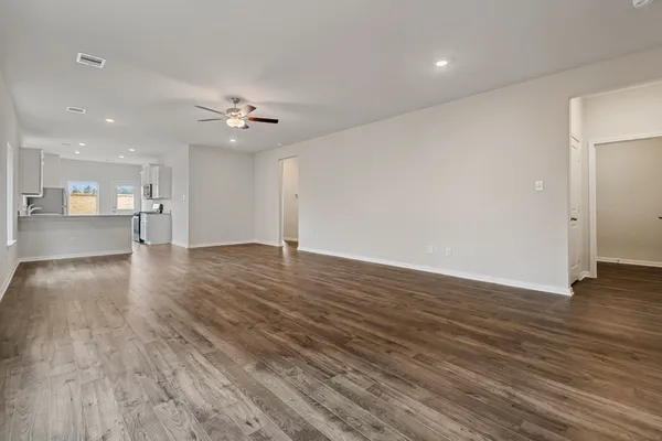 a view of an empty room with wooden floor and a kitchen