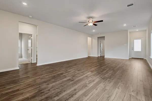 a view of an empty room with wooden floor and a ceiling fan