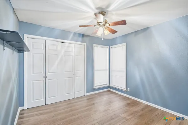 an empty room with wooden floor fan and windows