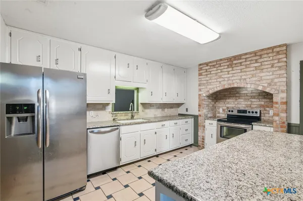 a kitchen with granite countertop a sink stainless steel appliances and white cabinets