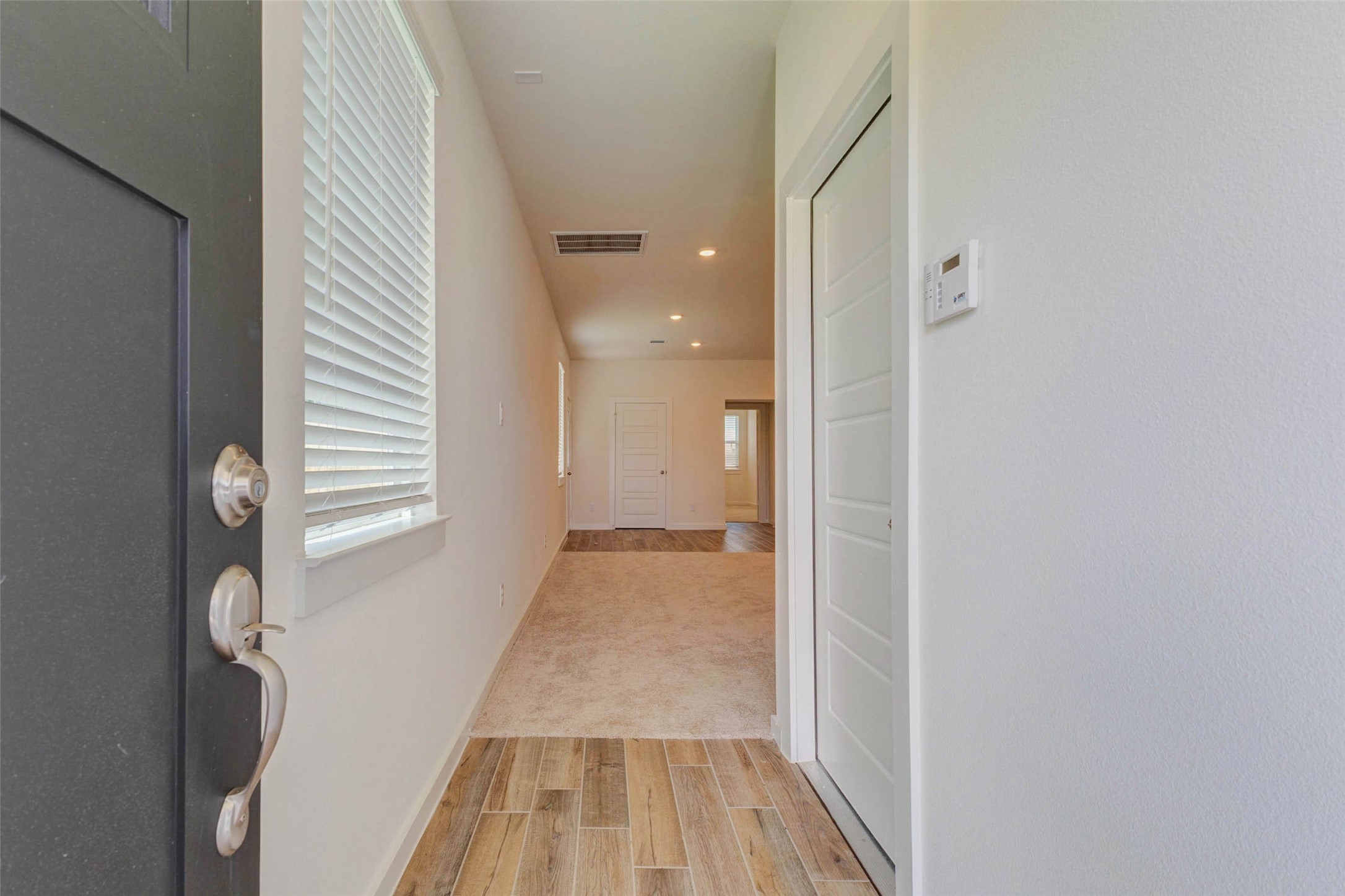 6471 Escondido Drive Rosharon, TX 77583 - Photo 9 of 33 Bright entryway with a black front door, window blinds, wood-look tile flooring, recessed lighting, and a long hallway leading toward the main living areas. The neutral color palette and clean finishes create an inviting first impression with a fresh, modern feel.