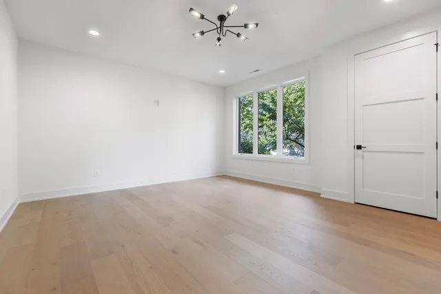 an empty room with wooden floor chandelier fan and windows