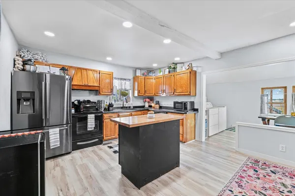 a kitchen with stainless steel appliances granite countertop a refrigerator a sink dishwasher a stove and a dining table with wooden floor