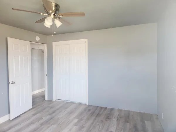an empty room with wooden floor fan and windows