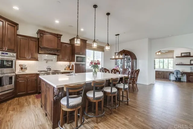 a kitchen with stainless steel appliances kitchen island granite countertop a stove a sink a dining table and chairs with wooden floor