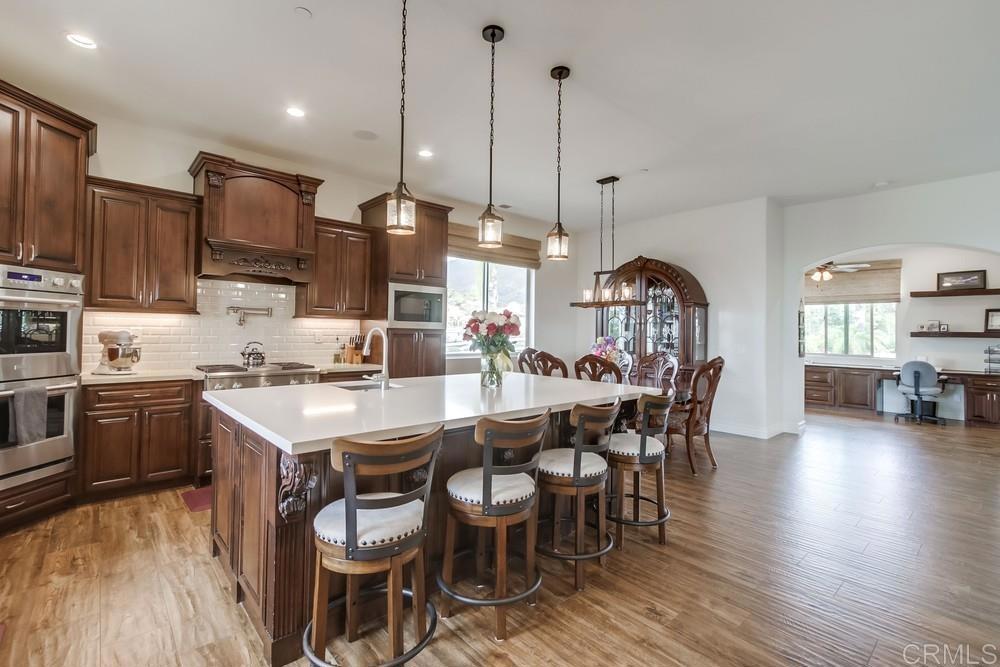 2893 Overland Passage Alpine, CA 91901 - Photo 15 of 51 a kitchen with stainless steel appliances kitchen island granite countertop a stove a sink a dining table and chairs with wooden floor