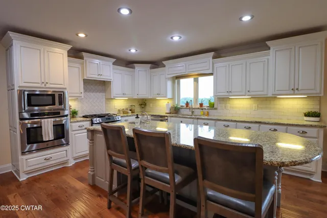 a kitchen with stainless steel appliances kitchen island granite countertop a table chairs sink refrigerator and cabinets