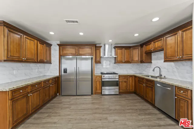 a kitchen with stainless steel appliances granite countertop a refrigerator a sink dishwasher a stove top oven and a center island with wooden floor