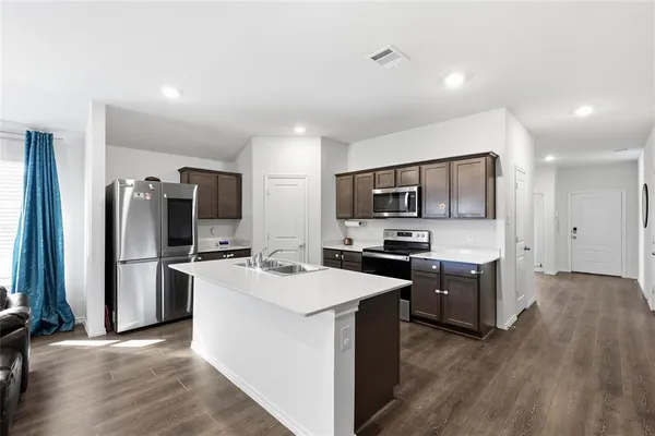 a kitchen with stainless steel appliances a stove top oven a refrigerator a sink a oven with wooden floor and cabinets