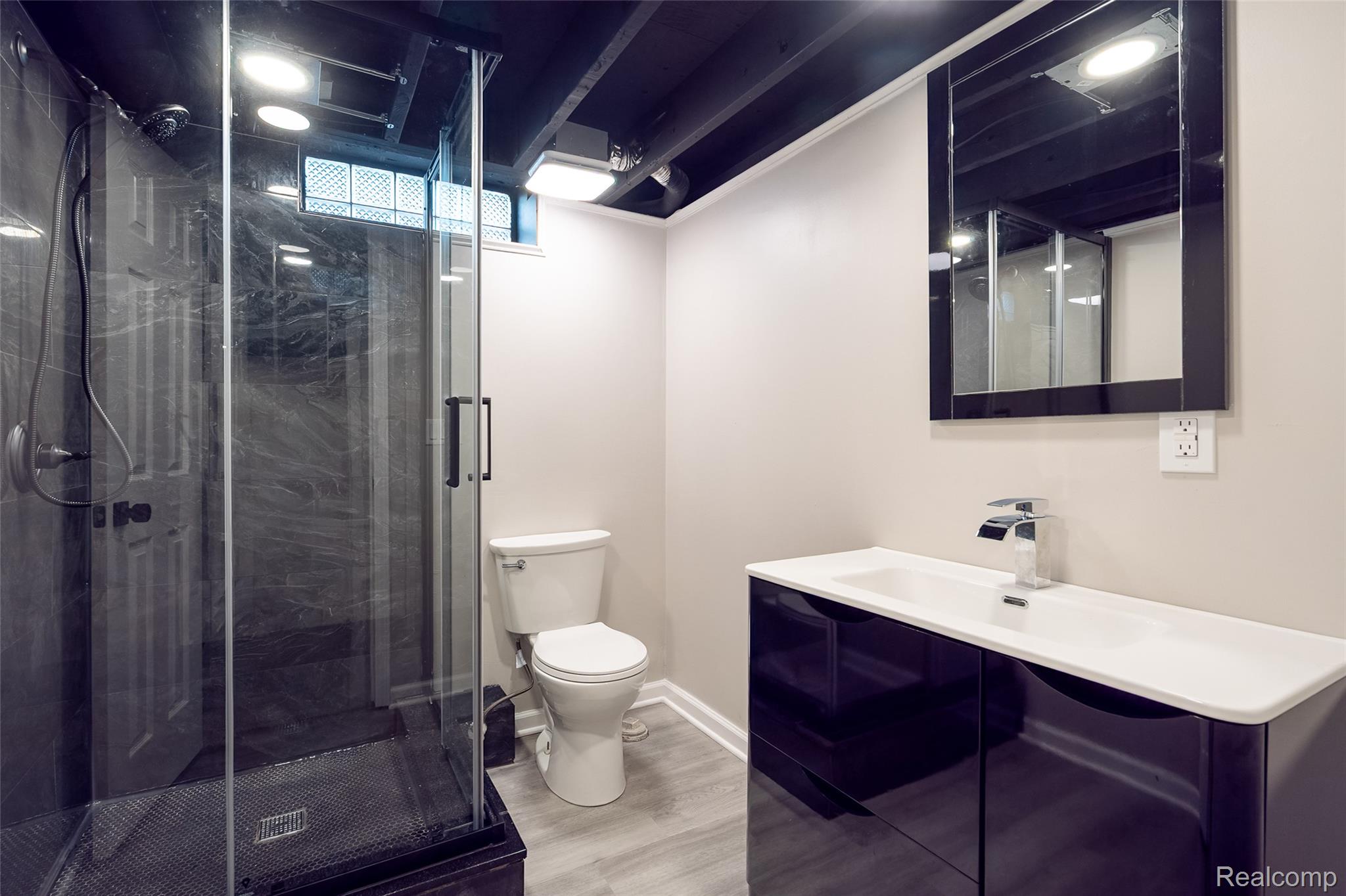 201 Cardwell Street Inkster, MI 48141 - Photo 34 of 41 Modern bathroom featuring a glass-enclosed shower with dark tile surround, a sleek vanity with an integrated sink, a contemporary mirror, and wood-finish flooring
