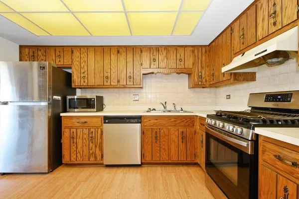 a kitchen with stainless steel appliances granite countertop a refrigerator a sink dishwasher a stove and white countertops with wooden floor