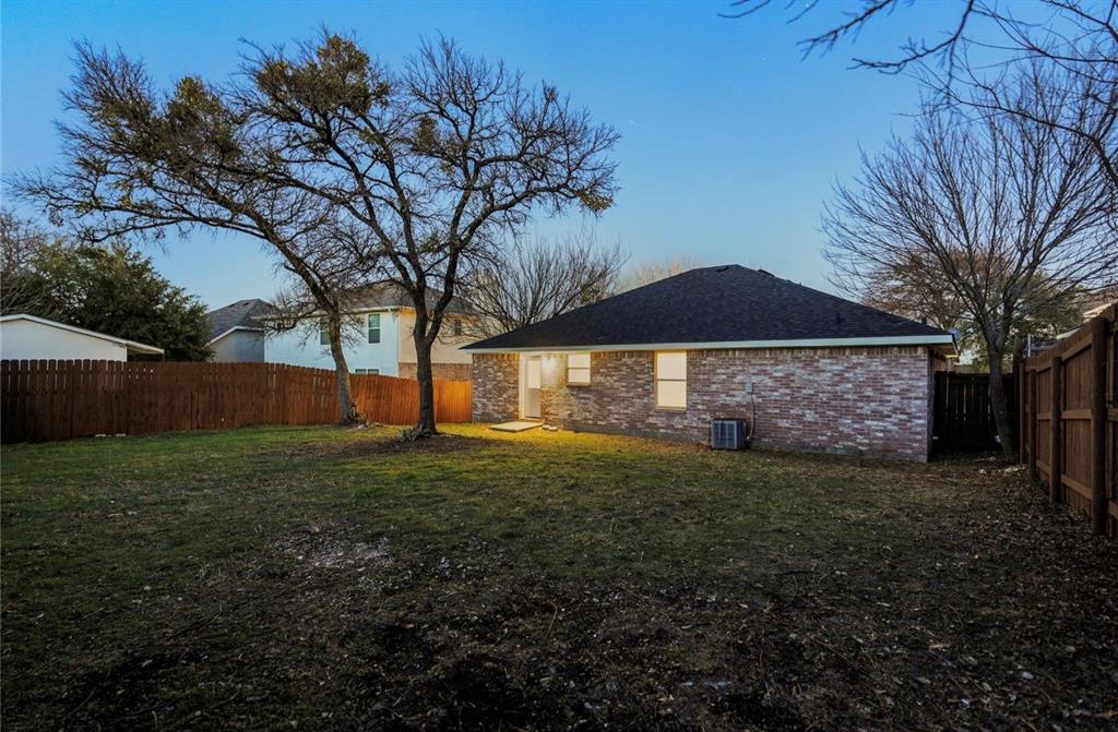 5169 East Rim Road Dallas, TX 75211 - Photo 6 of 19 Spacious backyard featuring a full privacy fence, mature trees, and a brick exterior with a dark shingle roof