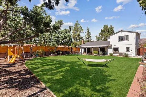 a view of a white house in front of a big yard with plants and large trees