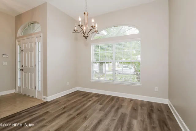 an empty room with wooden floor chandelier and windows