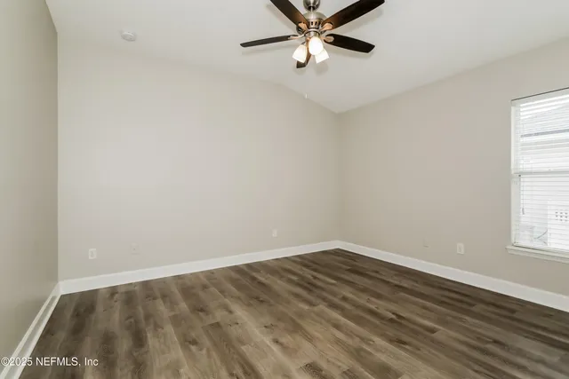 an empty room with wooden floor fan and windows