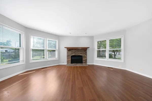 a view of an empty room with wooden floor windows and a fireplace
