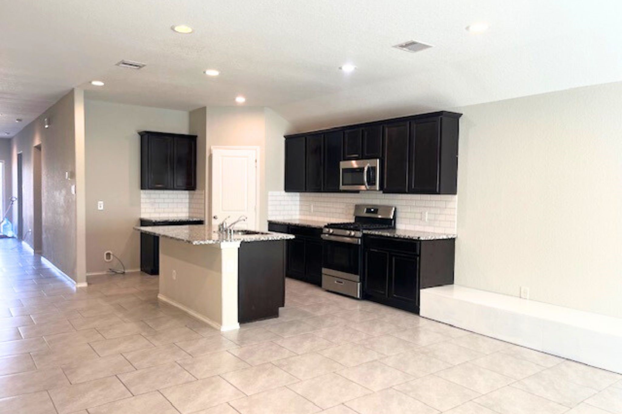 8310 Rose Petals Lane Rosharon, TX 77583 - Photo 4 of 43 Beautiful open-concept kitchen designed for both style and functionality, featuring a large granite island with built-in sink and breakfast seating. The kitchen is equipped with rich dark cabinetry, stainless steel appliances, a gas range, and elegant subway tile backsplash, creating a modern and timeless look. Recessed lighting and the open layout seamlessly connect the kitchen to the living and dining areas, making it perfect for everyday living and entertaining.