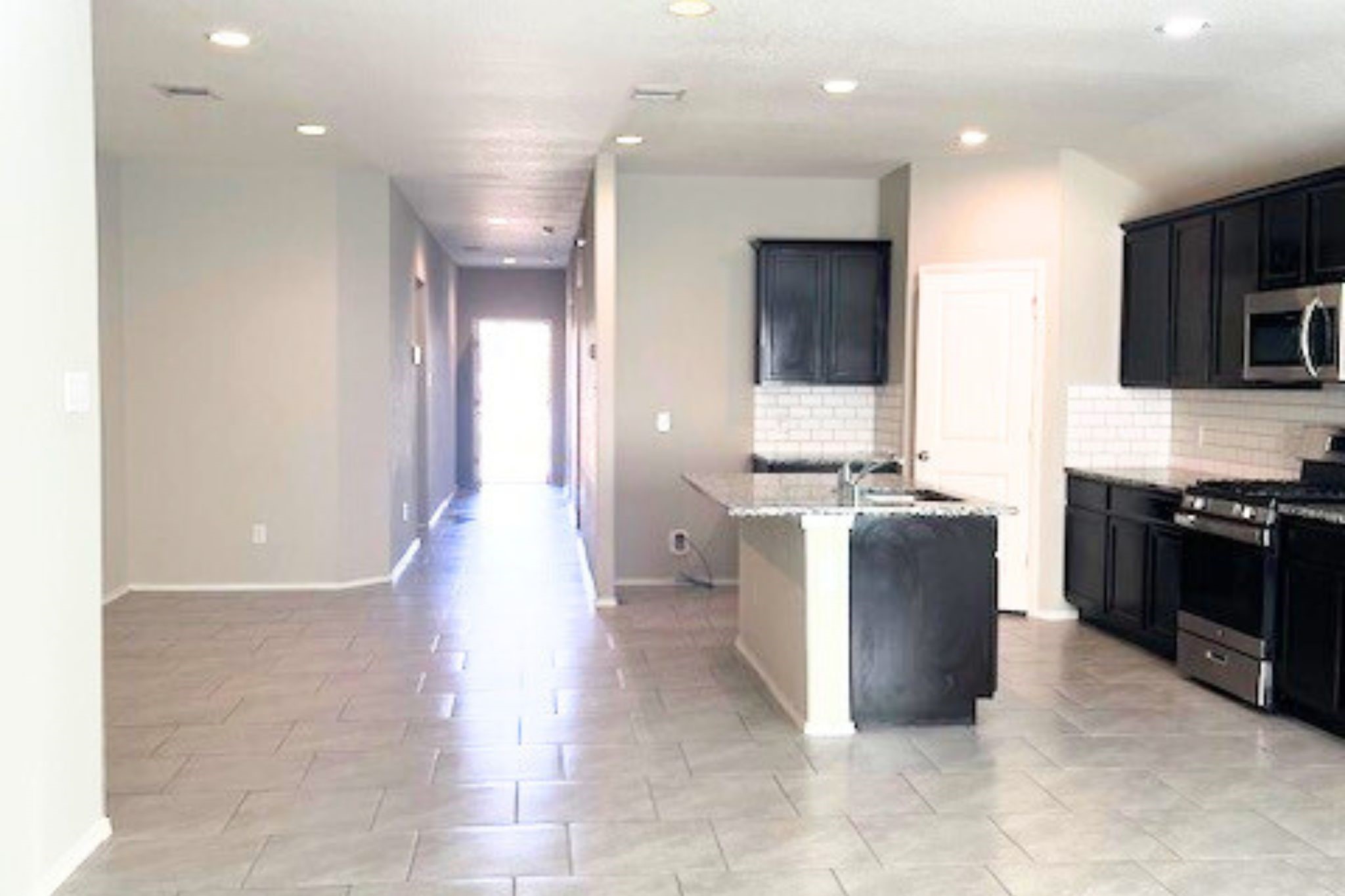 8310 Rose Petals Lane Rosharon, TX 77583 - Photo 7 of 43 Open and airy view from the kitchen looking toward the front entrance, showcasing the home’s spacious open-concept layout. The elegant tile flooring, recessed lighting, and seamless flow between the living, dining, and kitchen areas create a bright and welcoming atmosphere. This thoughtful layout provides a clear sightline from the kitchen to the entryway, enhancing both convenience and the home’s modern, connected design.