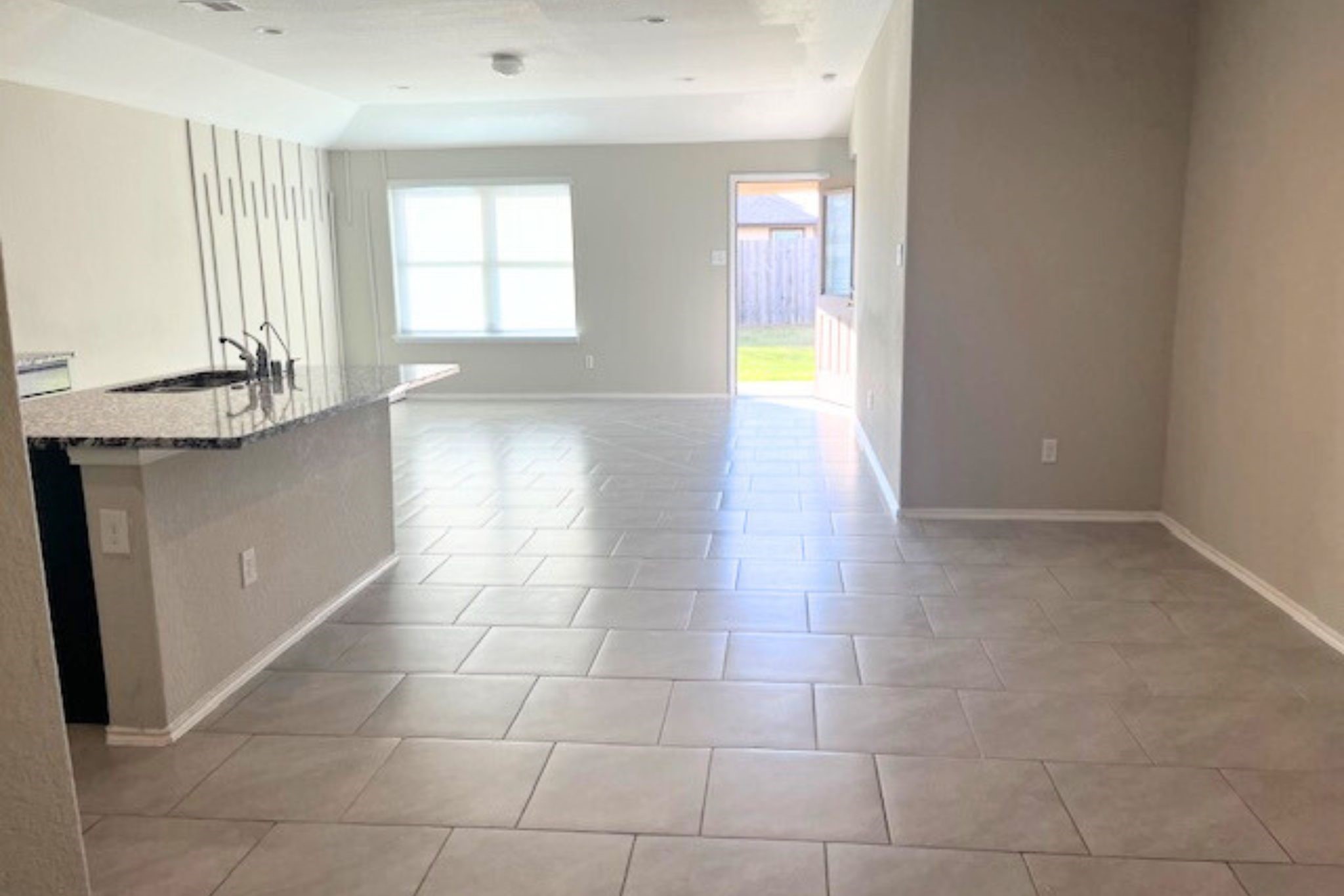 8310 Rose Petals Lane Rosharon, TX 77583 - Photo 9 of 43 Bright and spacious open-concept living area with a clear view toward the backyard, highlighting the home’s seamless indoor-outdoor flow. The elegant tile flooring, recessed lighting, and modern accent wall create a stylish and welcoming space. Large windows and the back door bring in natural light and provide easy access to the backyard, making this area perfect for relaxing, entertaining, and everyday living.