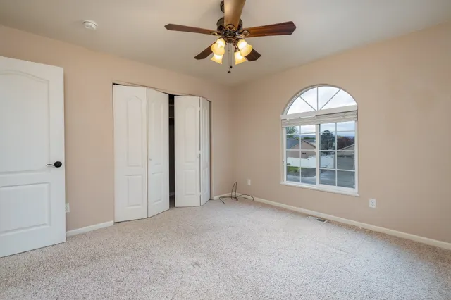 an empty room with chandelier fan and windows