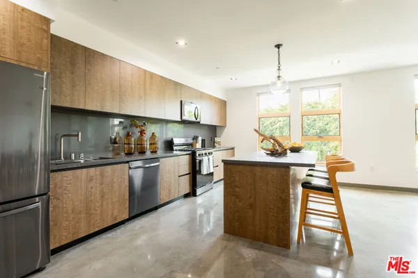 a kitchen with stainless steel appliances kitchen island granite countertop a refrigerator a sink dishwasher a stove and a dining table with wooden floor