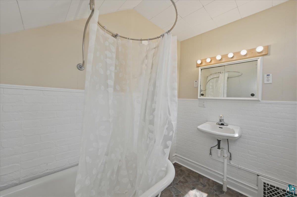 5319 East 3rd Street Superior, WI 54880 - Photo 30 of 33 Bathroom featuring a built-in tub with a curved shower rod, white brick-patterned wainscoting, a pedestal sink, and an illuminated medicine cabinet