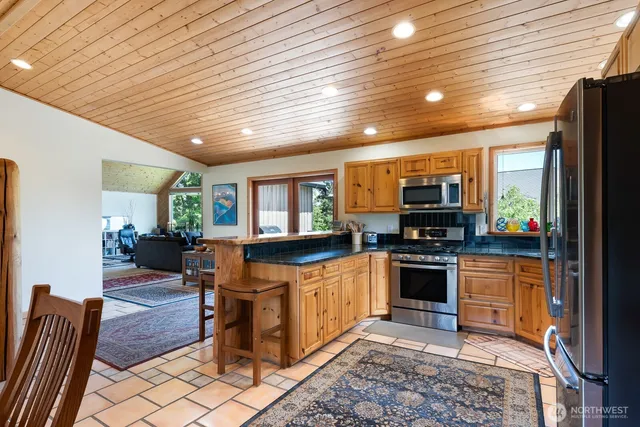 a kitchen with stainless steel appliances granite countertop a refrigerator a sink dishwasher a stove a dining table and chairs with wooden floor