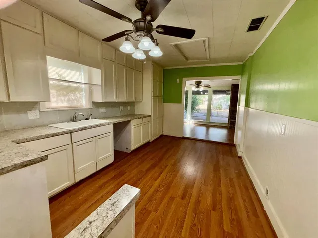 a large white kitchen with granite countertop a stove a sink and white cabinets with wooden floor