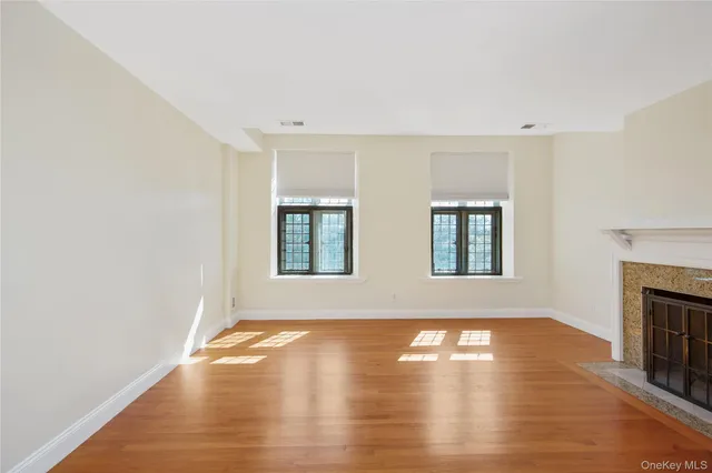 a view of an empty room with wooden floor fireplace and a window