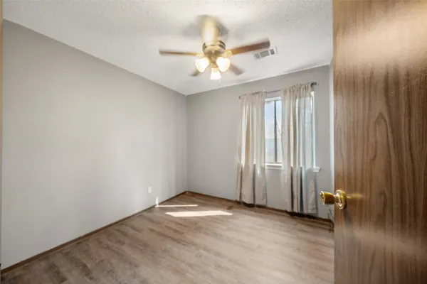an empty room with wooden floor fan and windows