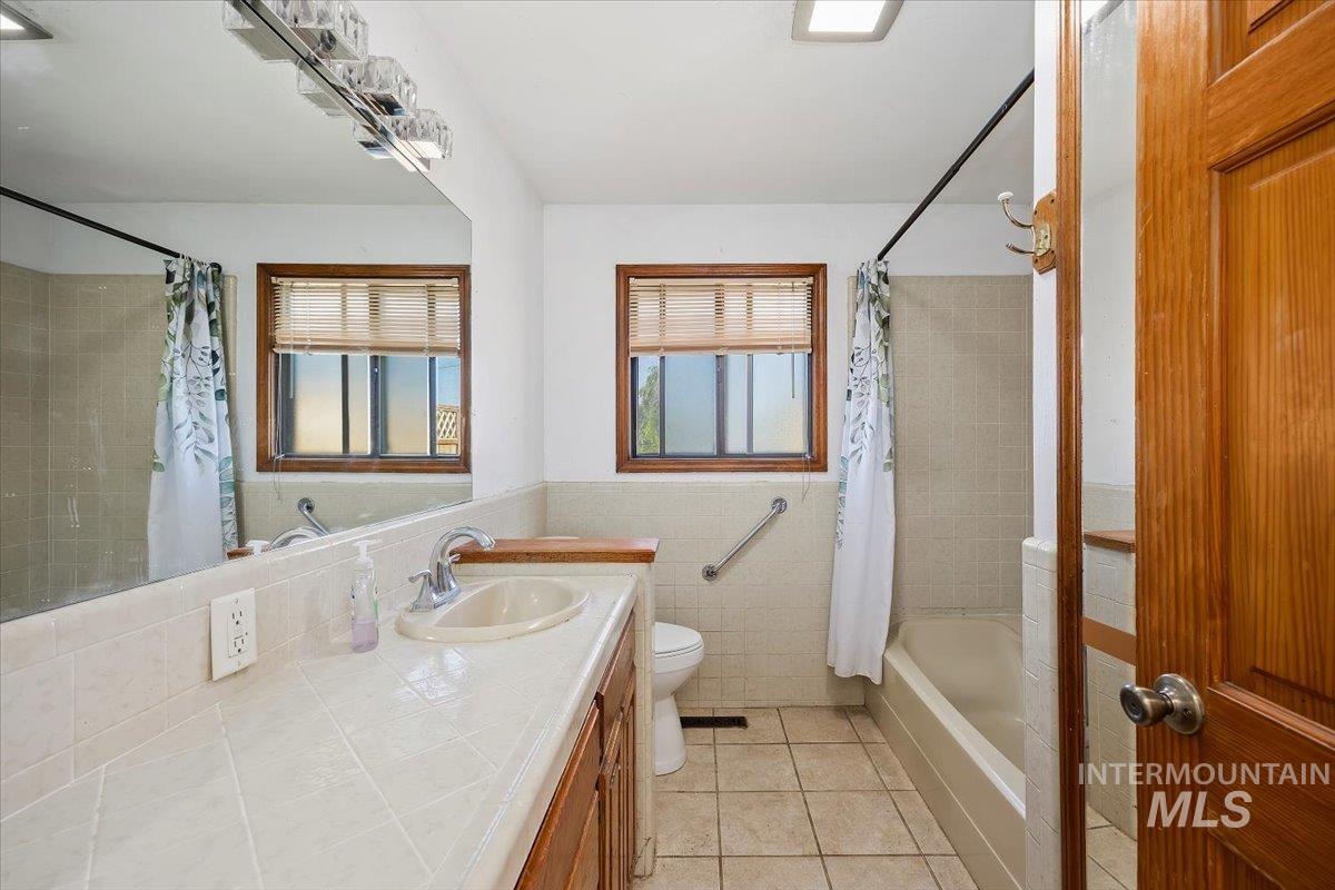 305 Lucille Street Kimberly, ID 83341 - Photo 21 of 36 Bathroom with vanity, tile patterned flooring, shower / bath combination with curtain, tile walls, and a wainscoted wall